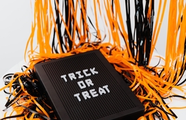 orange and black streamers behind a black board with white writing that says "Trick or Treat"