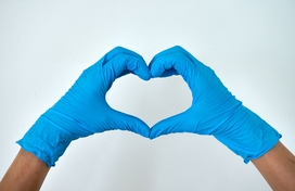 two blue-gloved hands form a heart shape in front of a white background