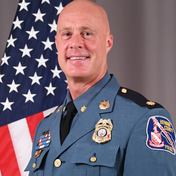 Major Thomas Ehart standing in front of flag