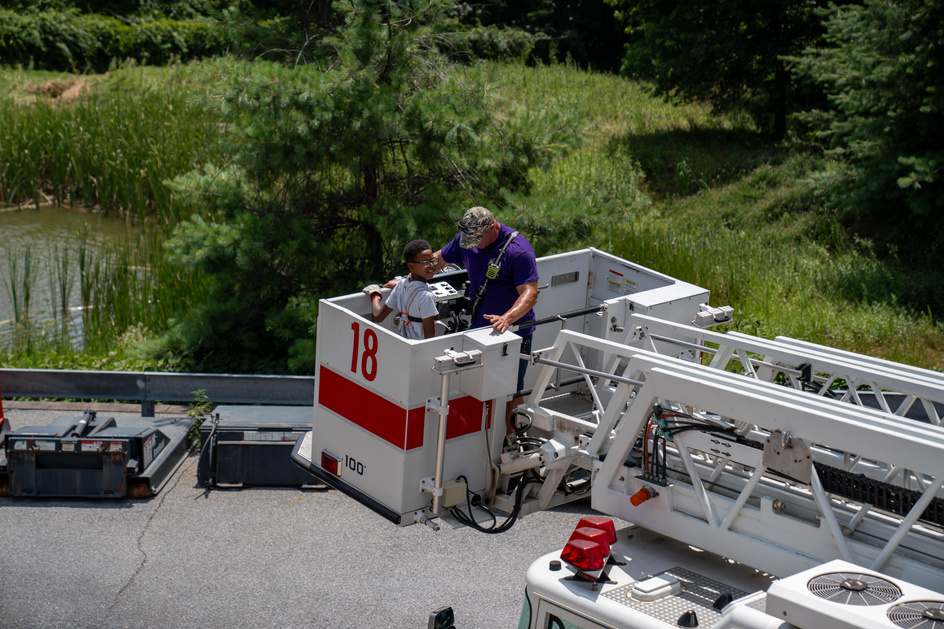 Camper joins firefighter in the extended bucket of a fire department apparatus.