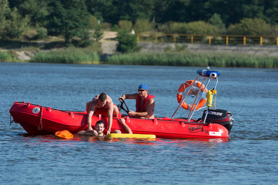 This image shows a water rescue scenario in which two individuals in a small red rescue boat assist a person in the water, helping them stay afloat using a flotation device.