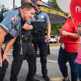 Uniformed officers interact with young girl holding a National Night Out Balloon