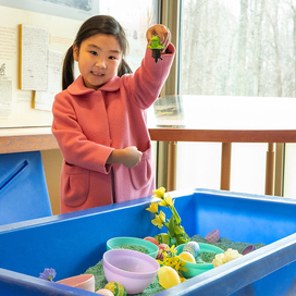 girl in pink coat holds up a toy