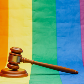 A wooden gavel resting on an LGBT Pride flag. 