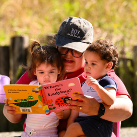 Two toddlers getting read a book by their mother. 
