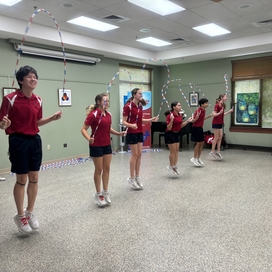 6 kids dressed in maroon shirts and black shorts doing a jump rope routine