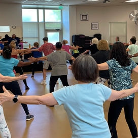 Group of older adults in an exercise class. They are facing away with their arms raised up to their sides.