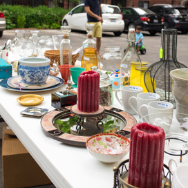 Table at yard sale with a variety of items including candles and mugs.