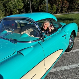 Older white woman sitting in the driver seal of a teal and cream colored classic car.