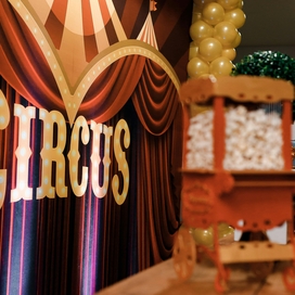 Maroon curtain with sign that says circus and a mini popcorn cart.
