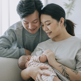 Asian Chinese young mother breastfeeding baby girl at home with father