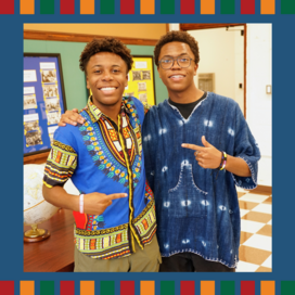 Two young people in traditional African clothing smile at the camera. 