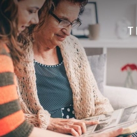 Two women, one older and one younger, sitting on a couch together looking over a handout. Trualta logo in the upper right hand corner of the photo.