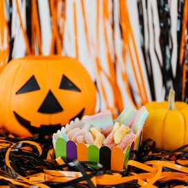 Pumpkin, plastic jack-o-lantern and cup of candy sitting atop black and orange streamers.