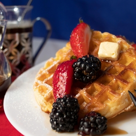 Waffles on a plate with strawberries and blackberries and syrup and butter.