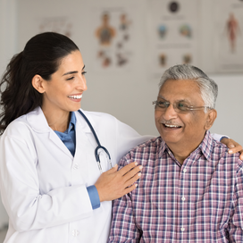 An older man with light brown skin is seen by a smiling doctor with long brown hair. 