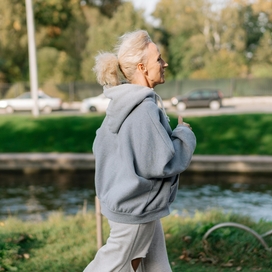 Caucasian women with light colored hair in pony tail running in a grey sweatshirt outside.