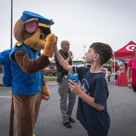 A person dressed as Chase from Paw Patrol high fives a child at National Night Out