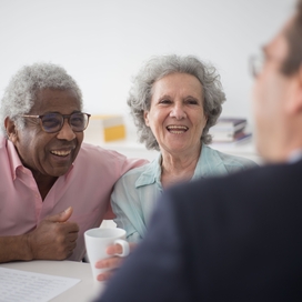 Black older adult male with Caucasian older adult female meeting with man at table.