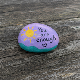 Rock painted with "You are enough". Also includes a sun and a heart.