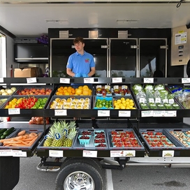 A man smiling standing outside in front of fruits and vegetables laid out in boxes
