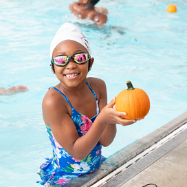 Smiling girl looking at camera holds pumpkin near edge of pool