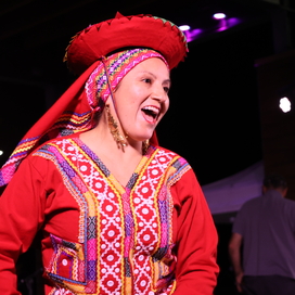 A woman in traditional Peruvian dress smiles while dancing on an outdoor stage. 