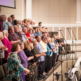 older adults singing on a tiered stage in front of an orchestra pit