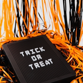 orange and black streamers behind a black board with white writing that says "Trick or Treat"